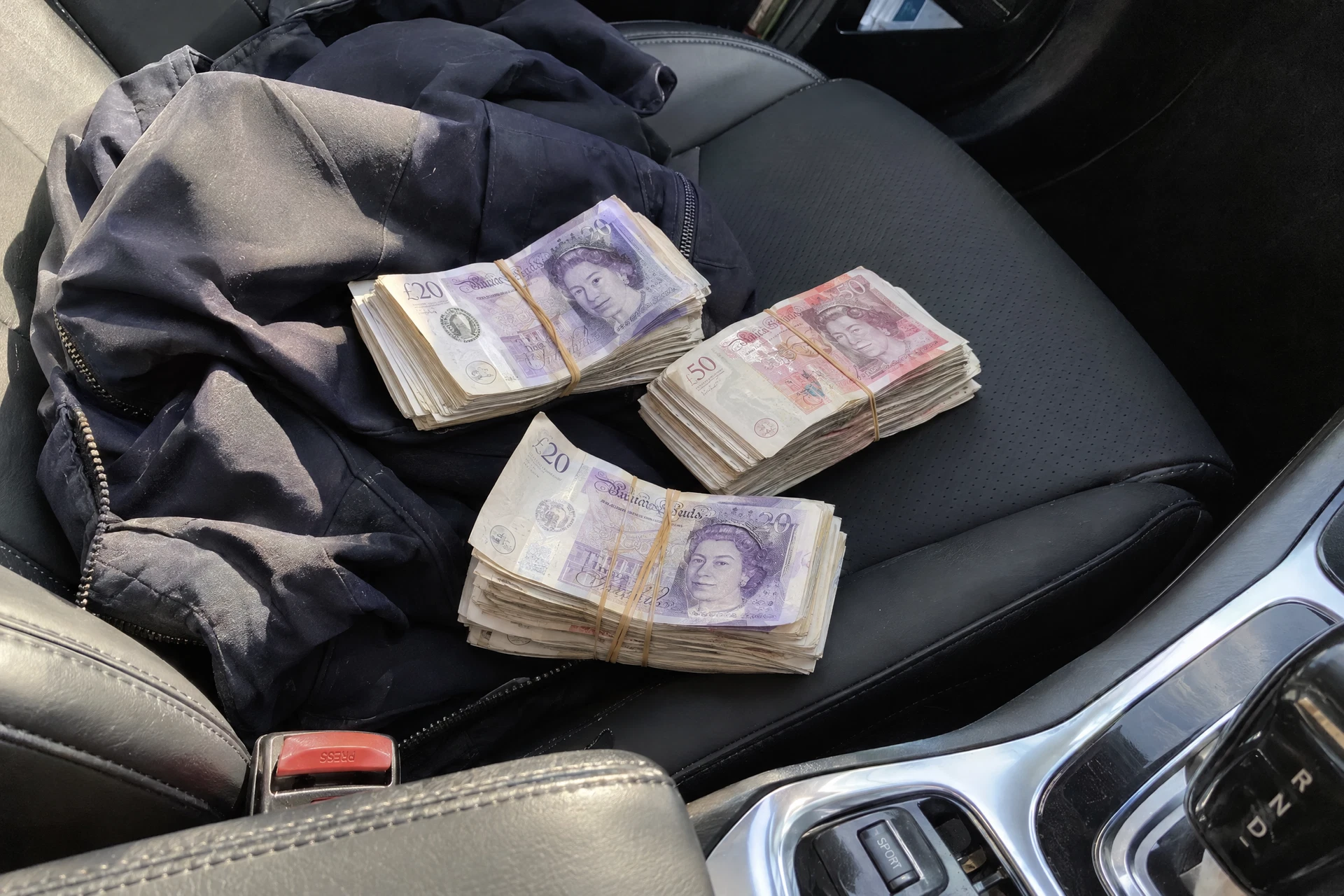 Illustrative scene of British pounds bundles held with rubber bands on a parked car’s passenger seat